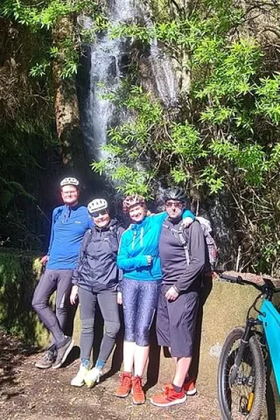 Group of riders posing by a small forest waterfall with their e-bike nearby on the Levada da Camacha Trail by E-Bike, an experience by Madeira Island Route.