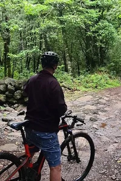 Rider with an e-bike pausing on a rocky forest path beside a stream crossing on the Levada da Camacha Trail by E-Bike, an experience by Madeira Island Route.