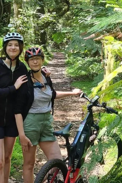 Two riders posing with their e-bike on a leafy forest path surrounded by ferns on the Levada da Camacha Trail by E-Bike, an experience by Madeira Island Route.