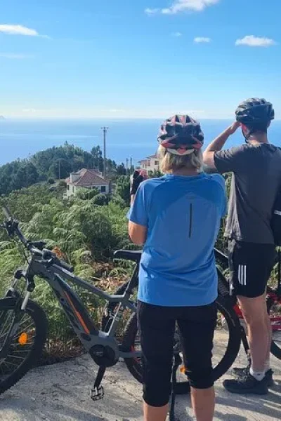 Group of riders with e-bikes enjoying a sunny viewpoint over the mountains and ocean on the Levada da Camacha Trail by E-Bike, an experience by Madeira Island Route.