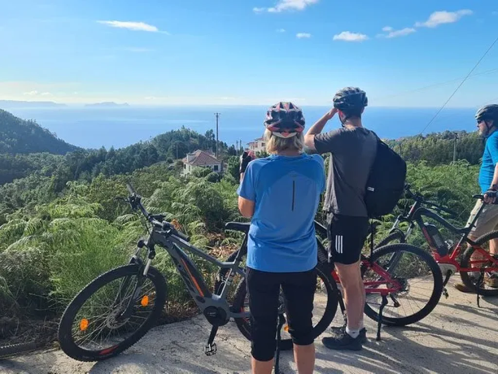 Group of riders with e-bikes enjoying a sunny viewpoint over the mountains and ocean on the Levada da Camacha Trail by E-Bike, an experience by Madeira Island Route.
