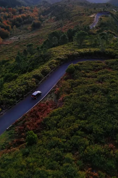 A top view photo of a Jeep on a road surrounded by green vegetation and mountains on the horizon, a view from the east of Madeira, Jeep Tour by Sea La Vie Mountain Expedition.