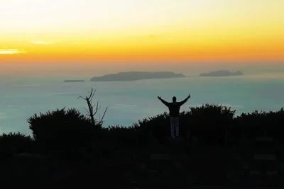 A man spreading his arms while contemplating the sunset over the sea, a view from the east coast of Madeira, an experience by Sea La Vie Mountain Expedition.