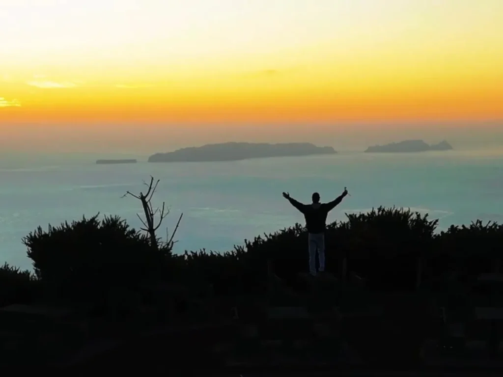 A man spreading his arms while contemplating the sunset over the sea, a view from the east coast of Madeira, an experience by Sea La Vie Mountain Expedition.