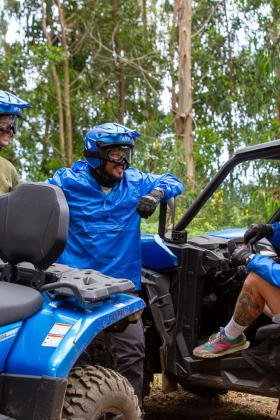 A close up of 4 People talking to each other near a blue buggy and an ATV with trees on the back during a Let's Buggy's Trail Thrill experience in Madeira.