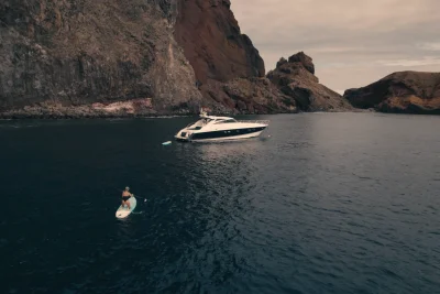 Luxury Madeira Yacht Charter Rental in the sea near the coast of Madeira and a woman on top of a paddle board rowing, an experience by Luxury Charter Madeira.