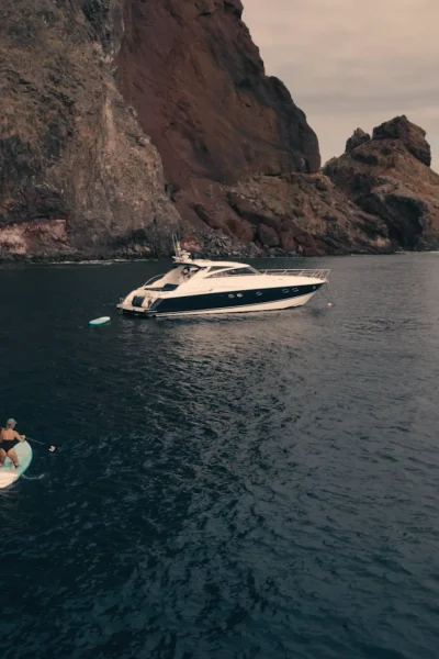 Luxury Madeira Yacht Charter Rental in the sea near the coast of Madeira and a woman on top of a paddle board rowing, an experience by Luxury Charter Madeira.