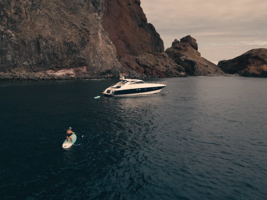 Luxury Madeira Yacht Charter Rental in the sea near the coast of Madeira and a woman on top of a paddle board rowing, an experience by Luxury Charter Madeira.
