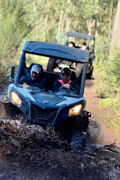 Buggy splashing through a muddy puddle on a forest trail near Câmara de Lobos, with another vehicle following behind among the green trees, during an adventure buggy tour by Madeira Radical.