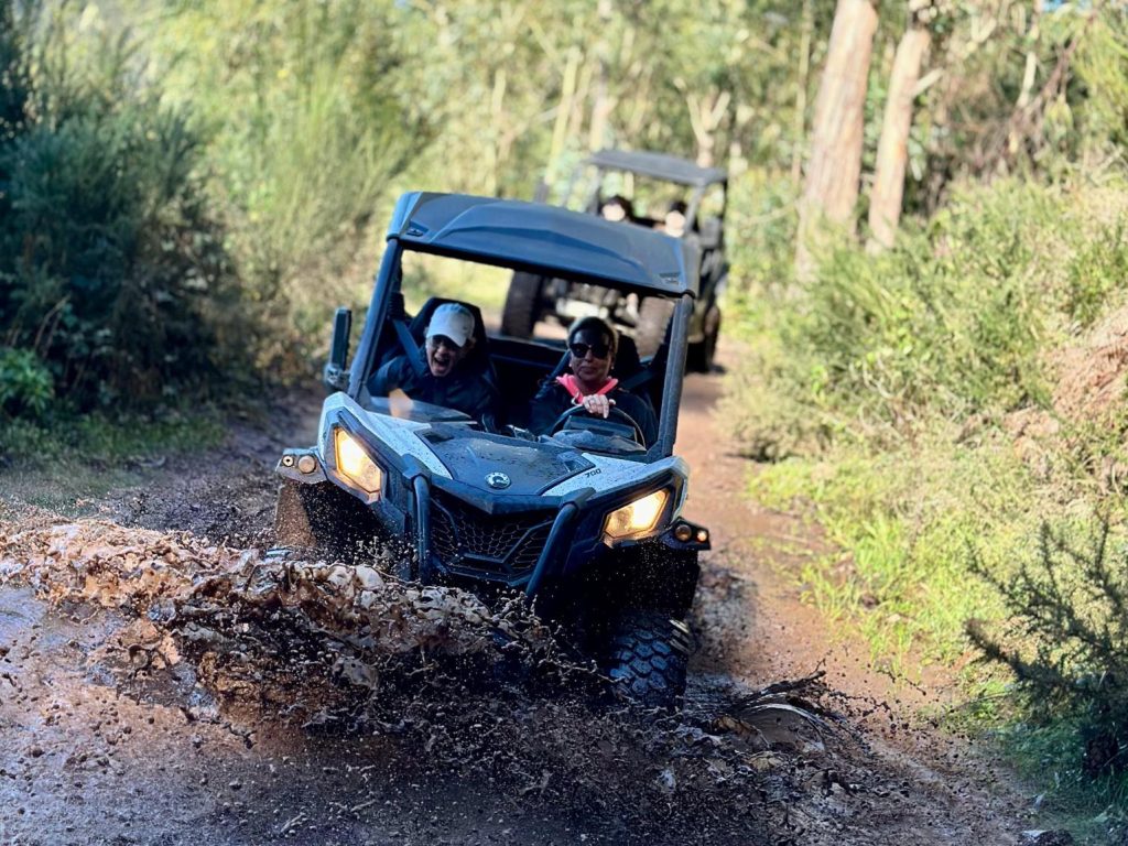Buggy splashing through a muddy puddle on a forest trail near Câmara de Lobos, with another vehicle following behind among the green trees, during an adventure buggy tour by Madeira Radical.