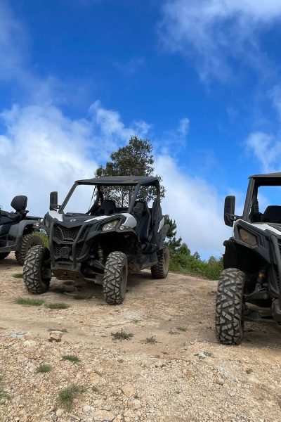 Two buggies and an ATV parked on a rocky hilltop under a bright blue sky, showcasing the off-road vehicles used on Madeira adventure tours by Buggy Funtrip Madeira.