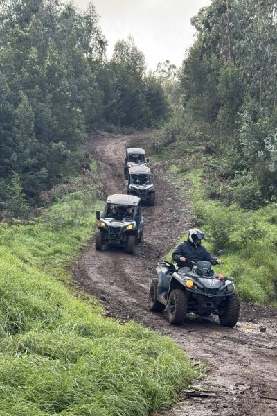 ATV leading a line of buggies down a narrow muddy trail, surrounded by dense green forest during an off-road adventure tour in Madeira by Buggy Funtrip Madeira.