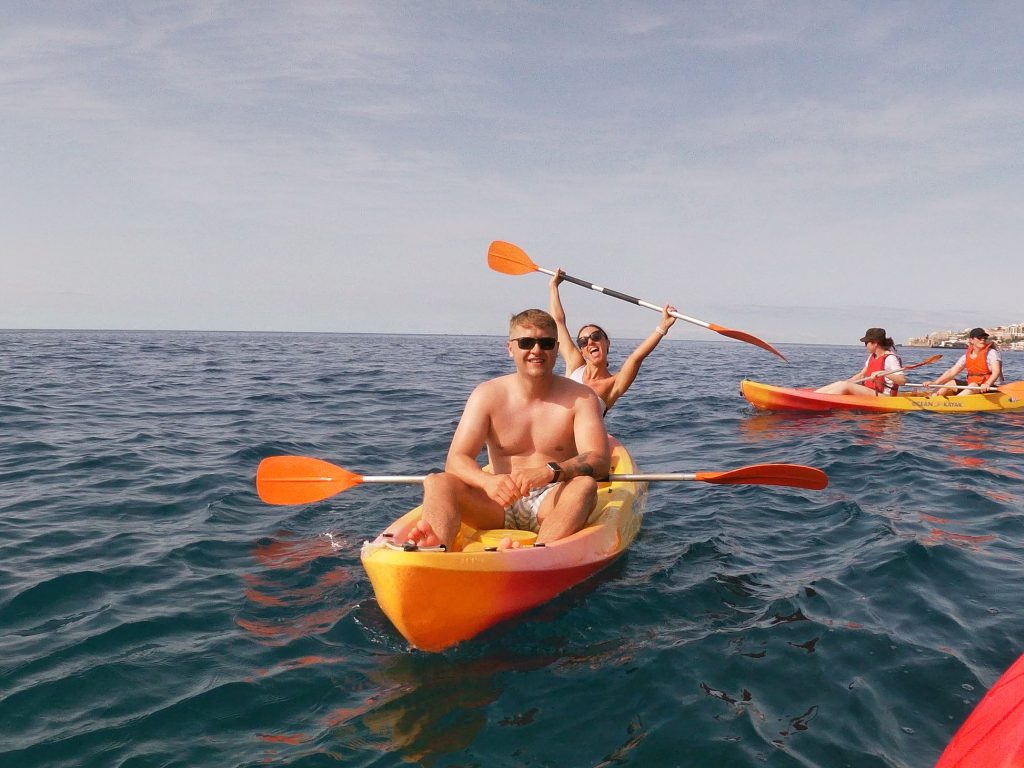 Couple kayaking on the ocean during a Madeira Radical Kayak Funchal Tour, an experience by Madeira Radical, with other participants paddling nearby on the calm blue water.