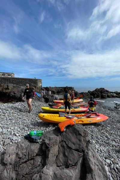 Group preparing colorful kayaks on a rocky beach in Madeira, with participants in life jackets getting ready to launch into the sea under a partly cloudy sky for an experience by Madeira Radical.