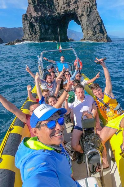 Group enjoying our 4h Day Pack fun in a boat tour at Ponta de São Lourenço, celebrating on a yellow speedboat in front of the iconic sea arch during a boat tour experience by Madeira Sea Emotions.