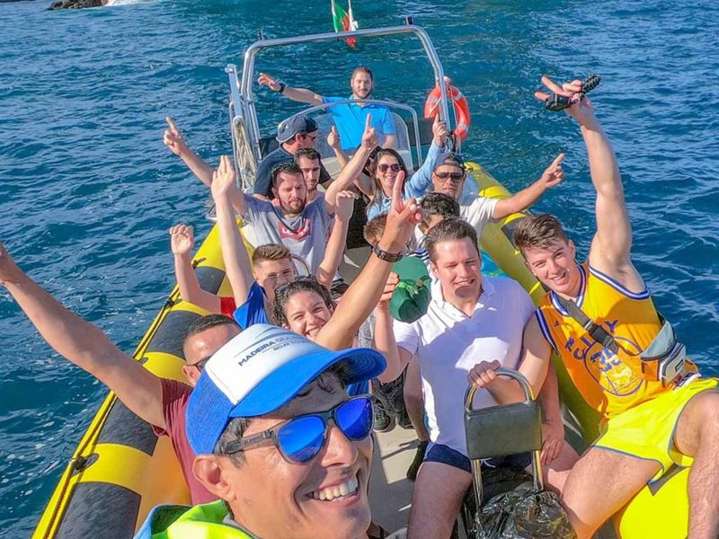 Group enjoying our 4h Day Pack fun in a boat tour at Ponta de São Lourenço, celebrating on a yellow speedboat in front of the iconic sea arch during a boat tour experience by Madeira Sea Emotions.