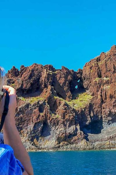 A close up of a woman on a Boat taking a picture of volcanic cliffs under sunny skies,a boat tour experience by Madeira Sea Emotions.