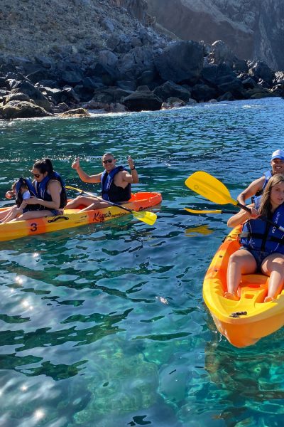 Two orange kayaks paddle along Ponta de São Lourenço's dark volcanic coastline, with life-vested explorers enjoying the turquoise waters and sunny skies, a Kayaking experience by Madeira Sea Emotions.