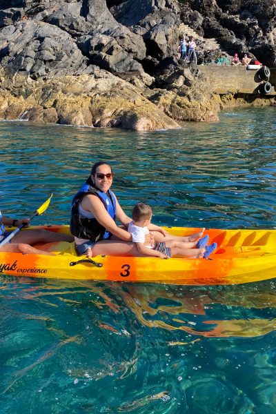 Two orange kayaks paddle alongalong Cais do Sardinha coastline, with life-vested explorers enjoying the turquoise waters and sunny skies, a Kayaking experience by Madeira Sea Emotions.