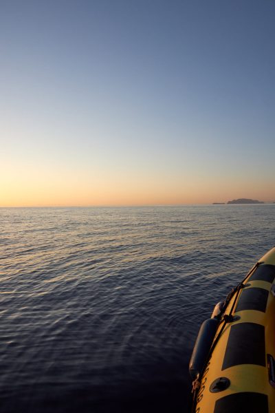 A yellow speedboat at sea during sunset, looking towards the Desertas Islands on a calm evening. During a boat tour, an experience by Madeira Sea Emotions.