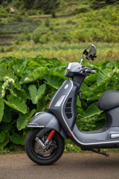 A grey Vespa parked and in the back green fields somwhere in Madeira.The type of scooter offered for rent to explore the Madeira island’s winding mountain roads and scenic viewpoints by Vespa Madeira Scooter Rent.
