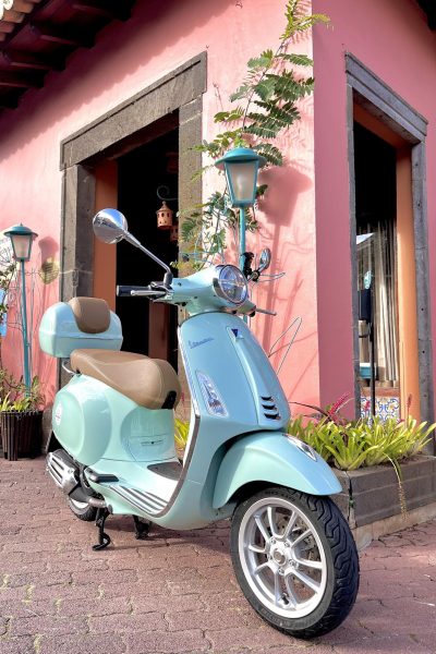 A green vespa parked near a pink house in Madeira. The type of scooter offered for rent to explore the Madeira island’s winding mountain roads and scenic viewpoints by Vespa Madeira Scooter Rent.