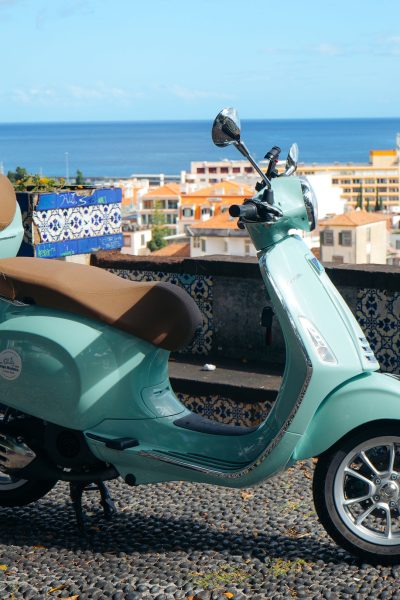 A green Vespa scooter is parked on a stone terrace, a funchal viewpoint in Madeira. The vehicle is a Vespa Primavera/GTS 125cc model, the type offered for rent to explore the island’s mountain roads and scenic viewpoints by Vespa Madeira Scooter Rent.
