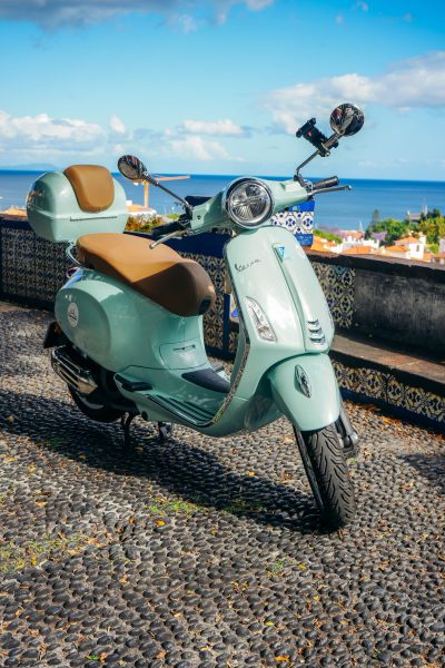 A green Vespa scooter is parked on a stone terrace, a funchal viewpoint in Madeira. The vehicle is a Vespa Primavera/GTS 125cc model, the type offered for rent to explore the island’s mountain roads and scenic viewpoints by Vespa Madeira Scooter Rent.