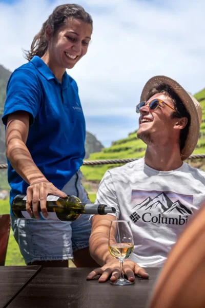 Smiling man being served a glass of white wine with terraced vineyards behind, an experience by Wine Tours Madeira