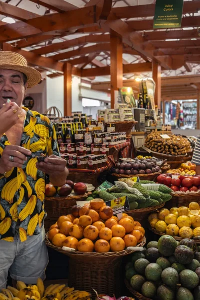 Group enjoying exotic fruit tastings and laughing together at a vibrant market stall during the Wine and Food Walking Tour in Funchal, an experience by Wine Tours Madeira.