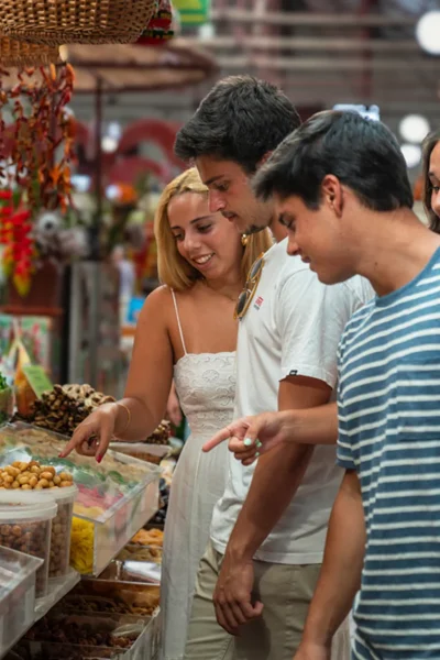 Guests sampling dried fruits and local snacks at a colorful Funchal market stall during the Wine and Food Walking Tour in Funchal, an experience by Wine Tours Madeira.