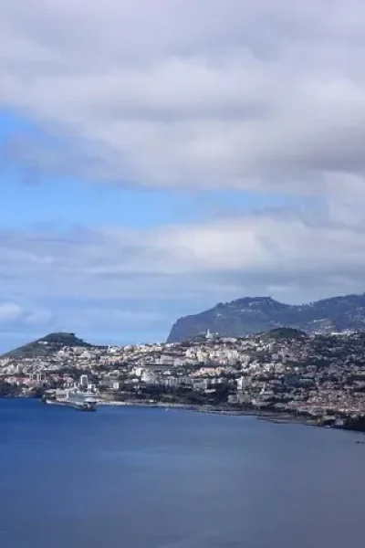 Funchal spread along the coast seen from a cliff across the bay under a cloudy sky